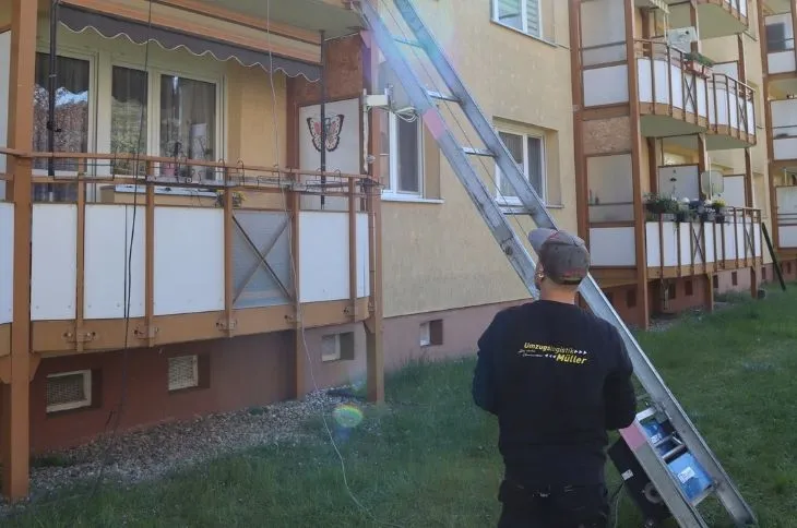 umzugshelfer bedient moebellift vor mehrfamilienhaus